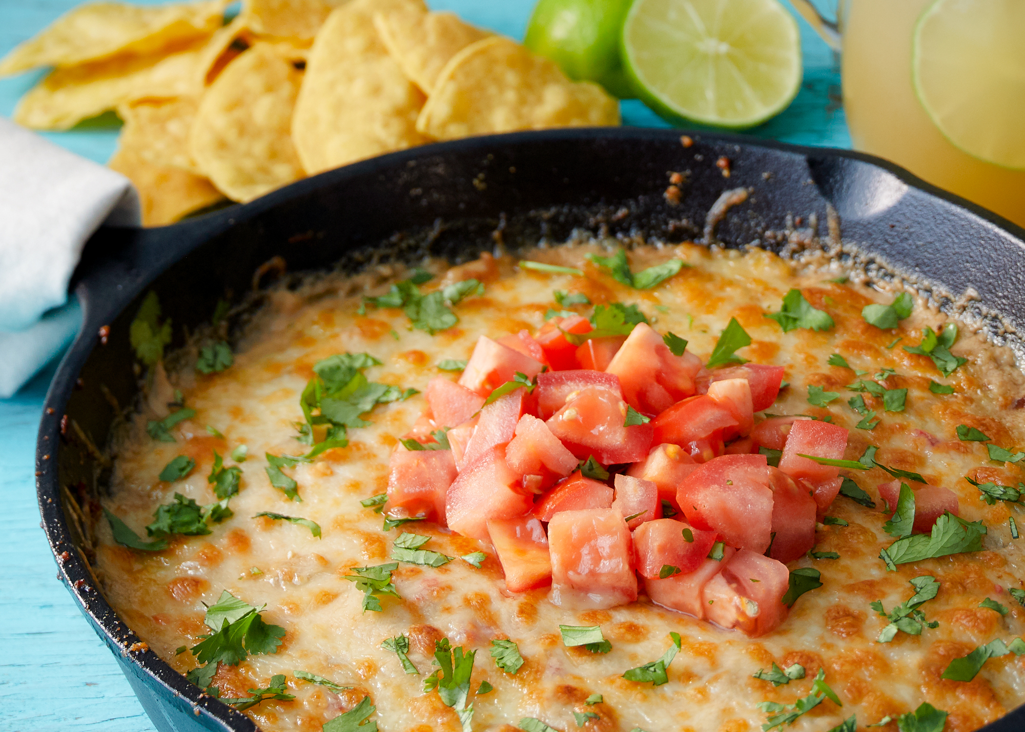 image of the Ghost Pepper Queso Dip in a cast iron skillet next to some chips and limes