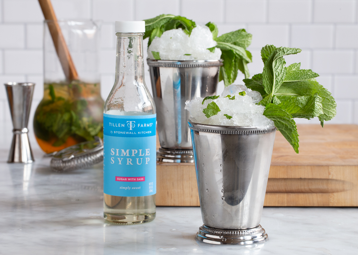 image of Tillen Farms Simple Syrup in a bottle on a kitchen counter next to two metal cups full of Mint Julep and crushed ice