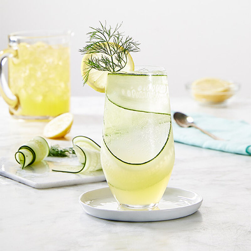 image of a glass of light green lemon cucumber aqua fresca with a thinly sliced cucumber in it and a small garnish at the top