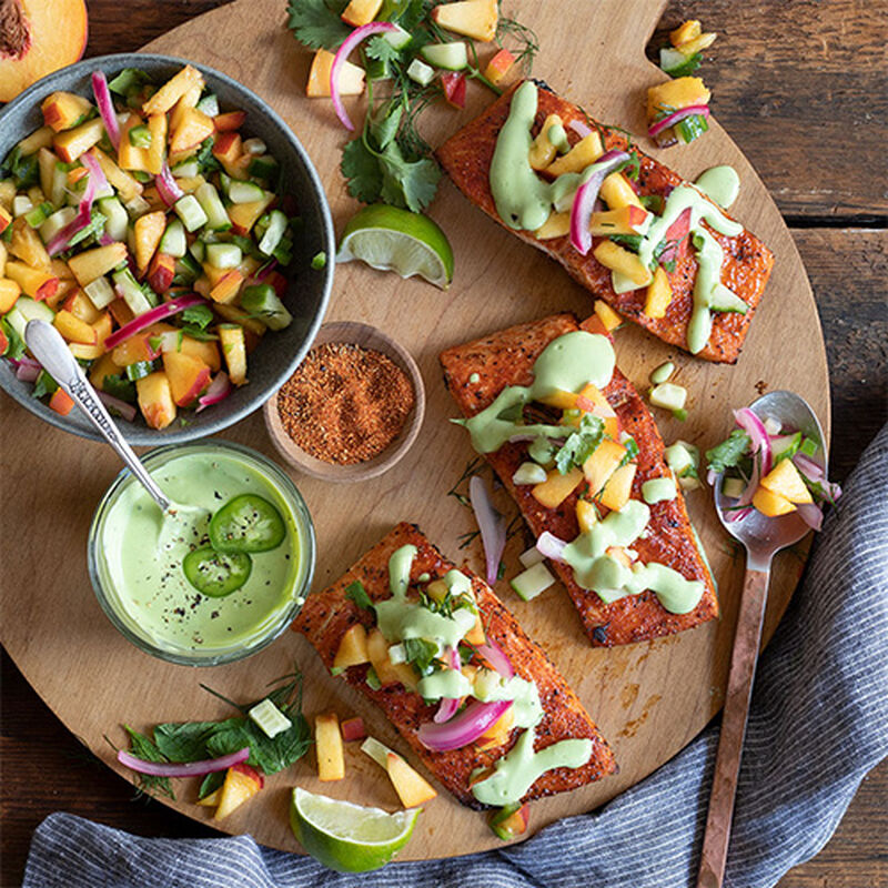 top-down image of plate with B.B.Q. glazed salmon with a heavy topping of peach salsa with garnishes, dipping sauce, and and spices on a rustic wooden counter