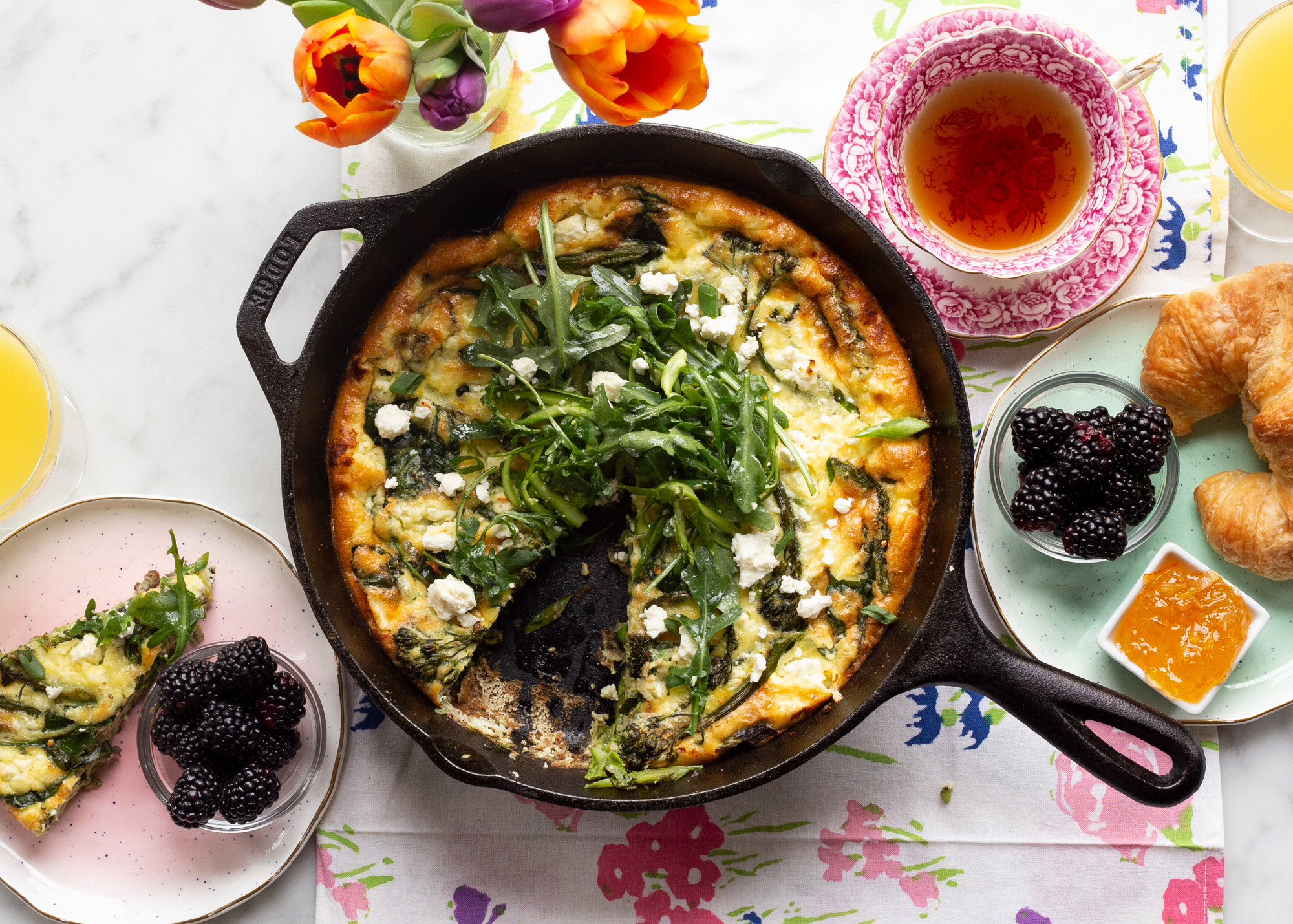 image of our Spring Veggie Fritata in a cast iron skillet on a table next to some tea and other brunch items like croissants