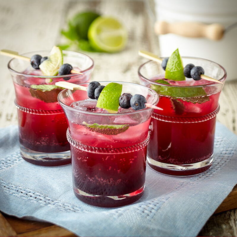 image of three glasses of purplish red blueberry mojito mocktails each with little blueberry and lime garnishes on a light blue napkin