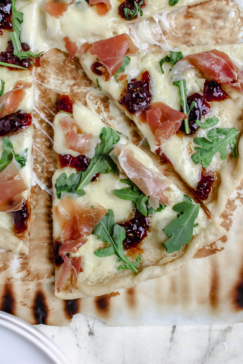 A top-down image of a prosciutto, brie, and fig jam pizza with a few pieces pulled out to show the melty cheese.