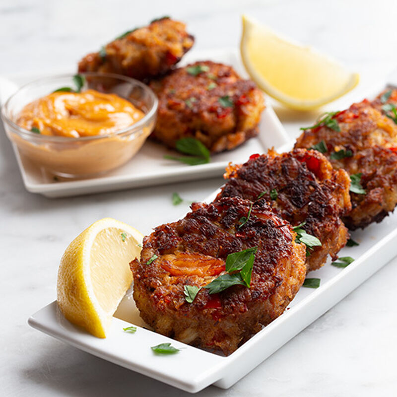 image of some long white rectangular plates with crab cakes on them lemons are included for garnishing and a bowl of aioli is included for dipping