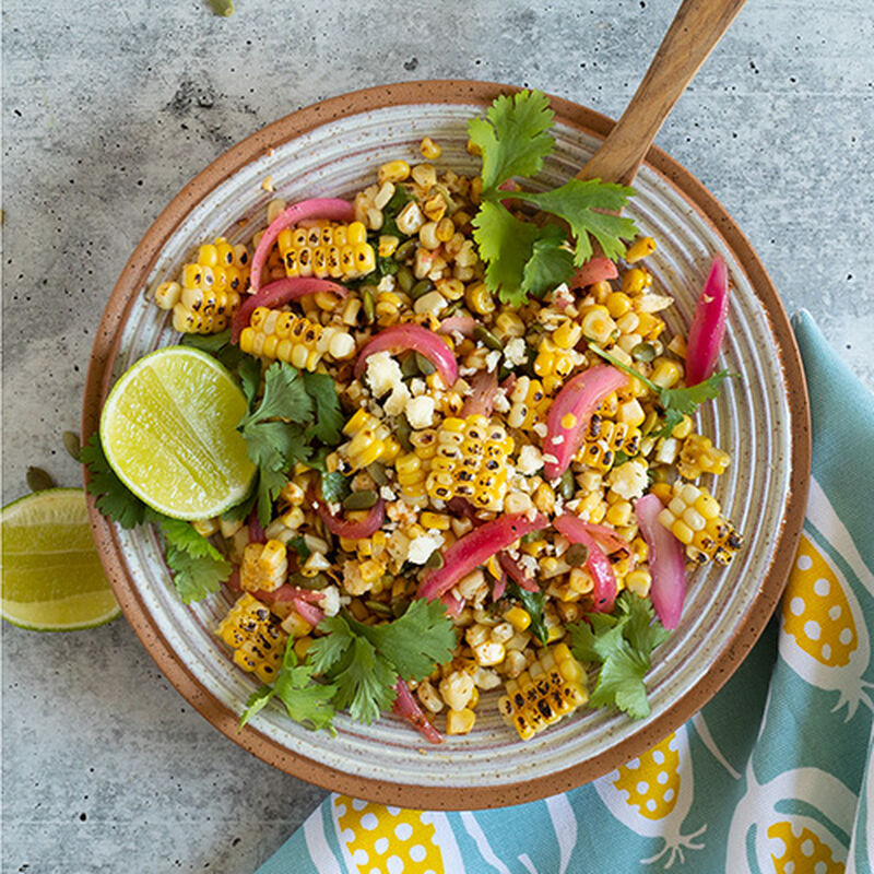 top-down image of a color plate of summer grilled corn salad with garnish and limes on a stone counter