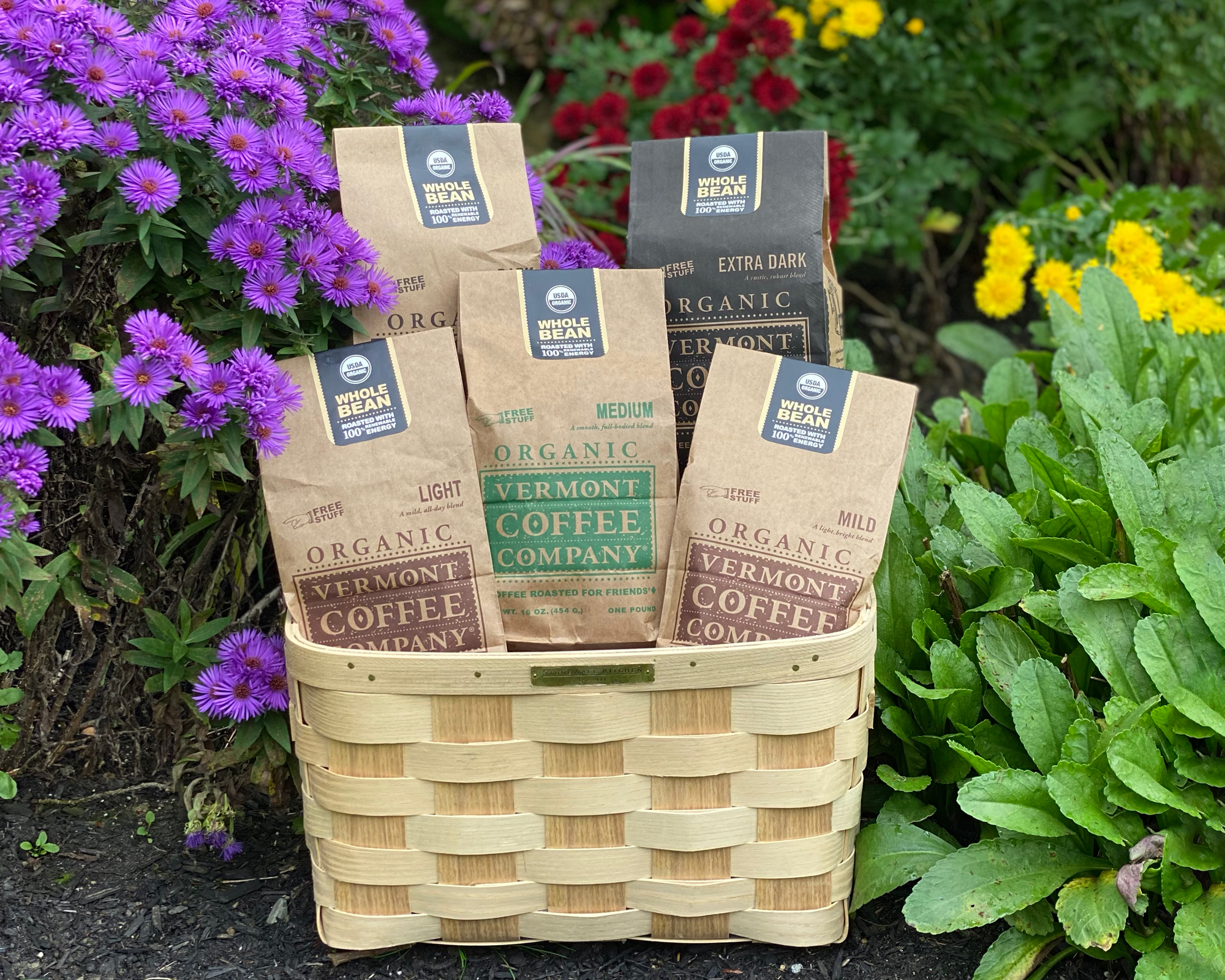 A wicker basket with five bags of Vermont Coffee Company coffee surrounded by flowers