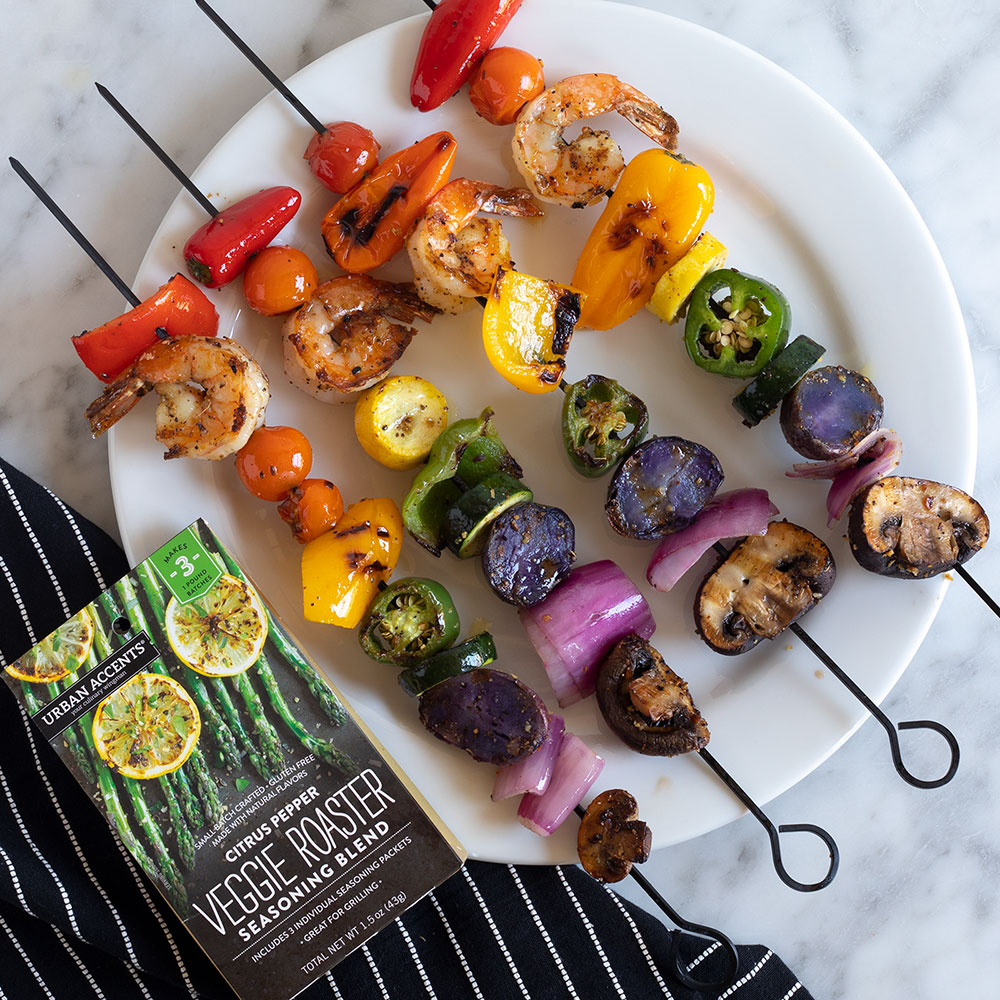 An image of five rainbow kabobs on a plate with a package of the Citrus Pepper Veggie Roaster next to it