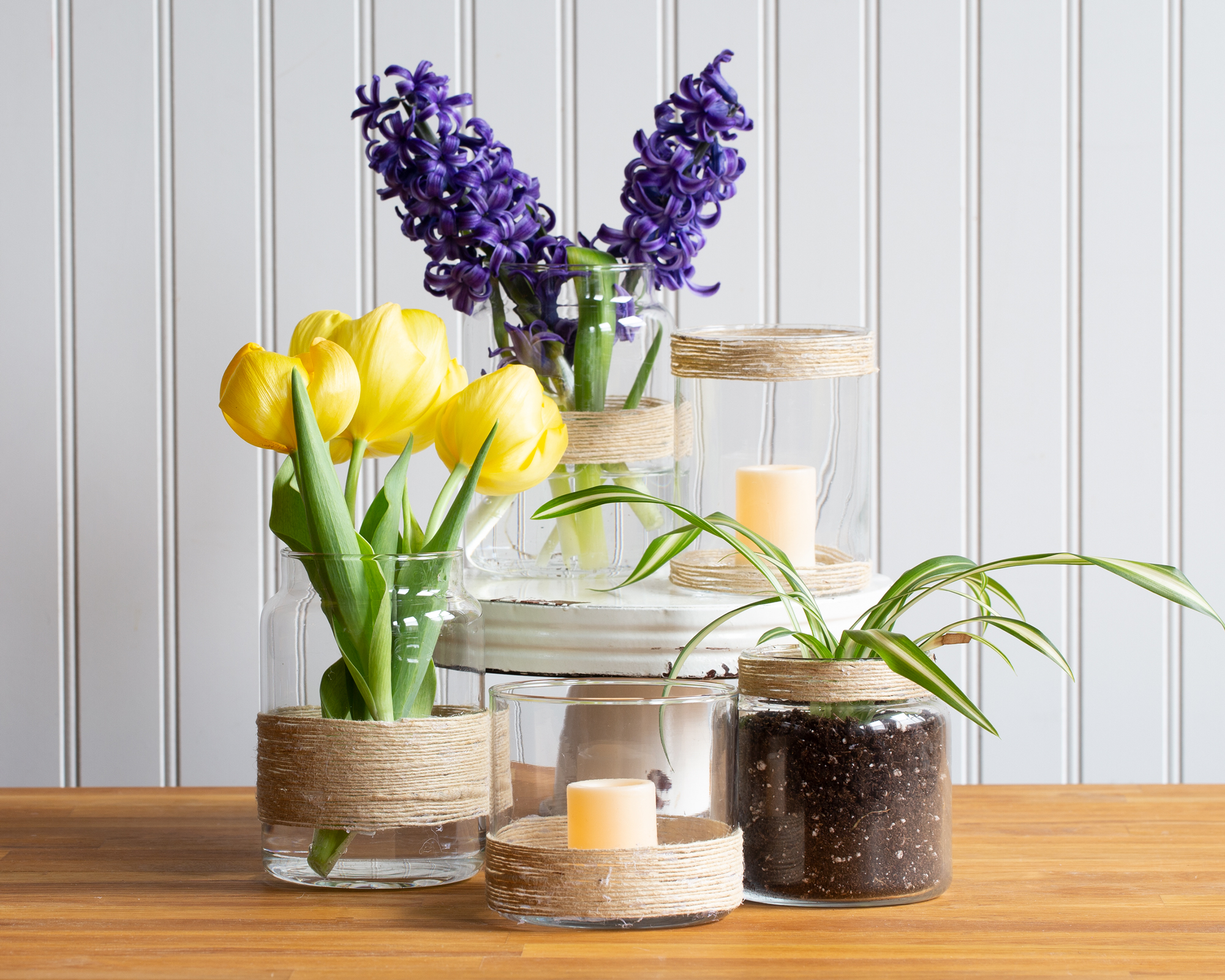 Five decorated jars on a counter containing flowers or candles