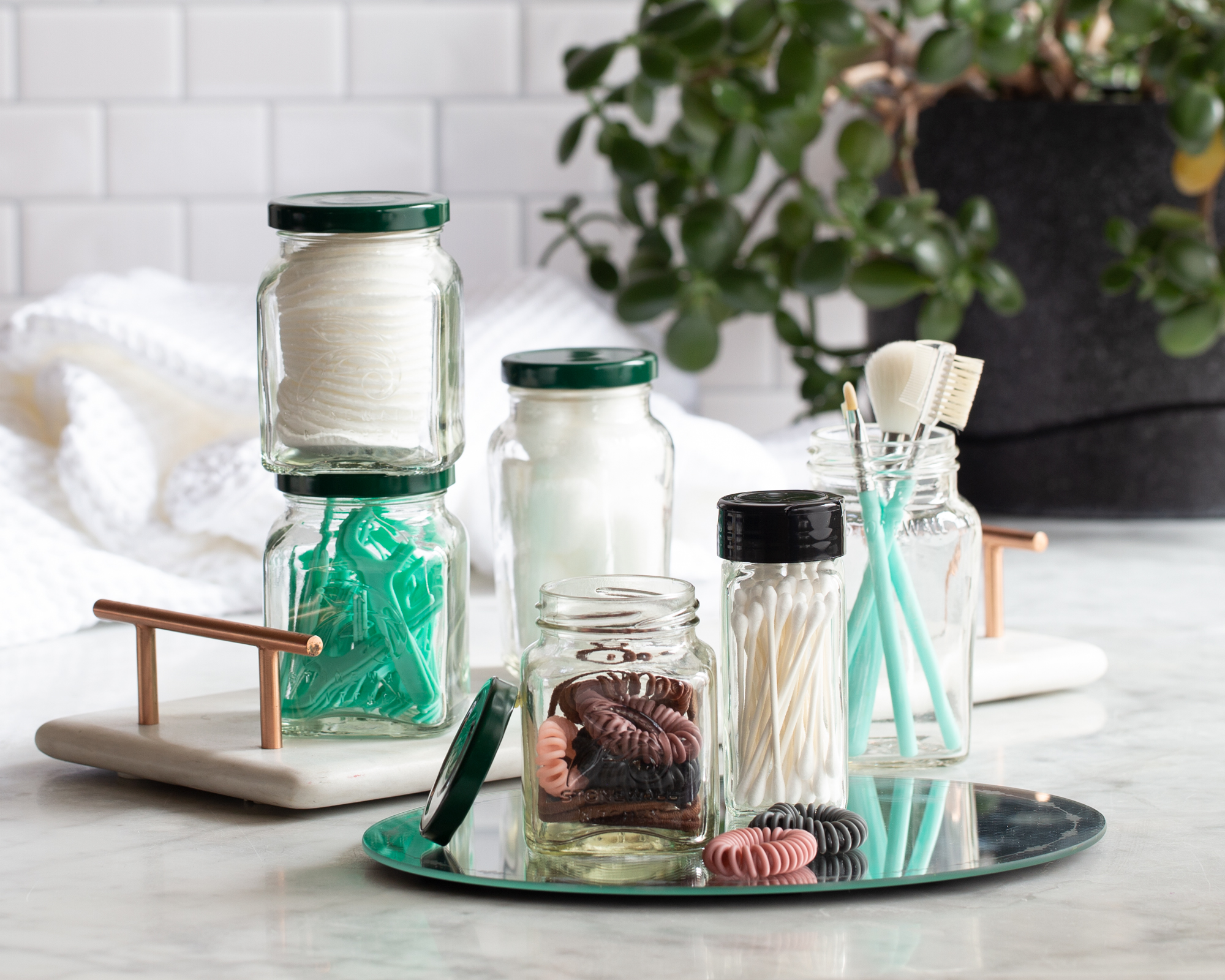 Six jars filled with various things like floss, twine, and cotton swabs in a bathroom on a counter