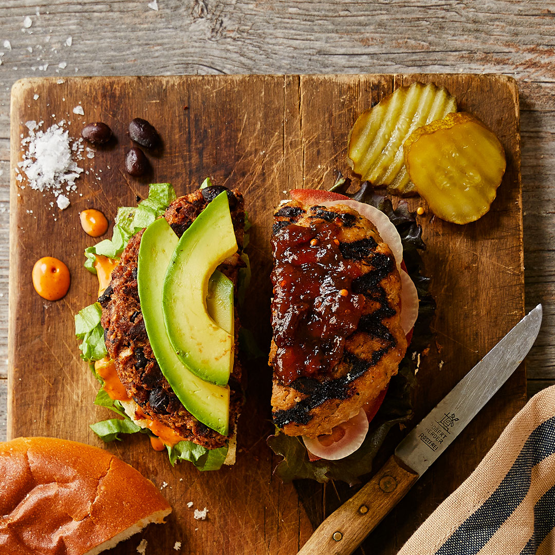 An image of a rustic serving board with a baked brie covered in chutney and bacon pieces flanked by crackers, berries and an open jar of chutney, all on a light gray granite countertop.